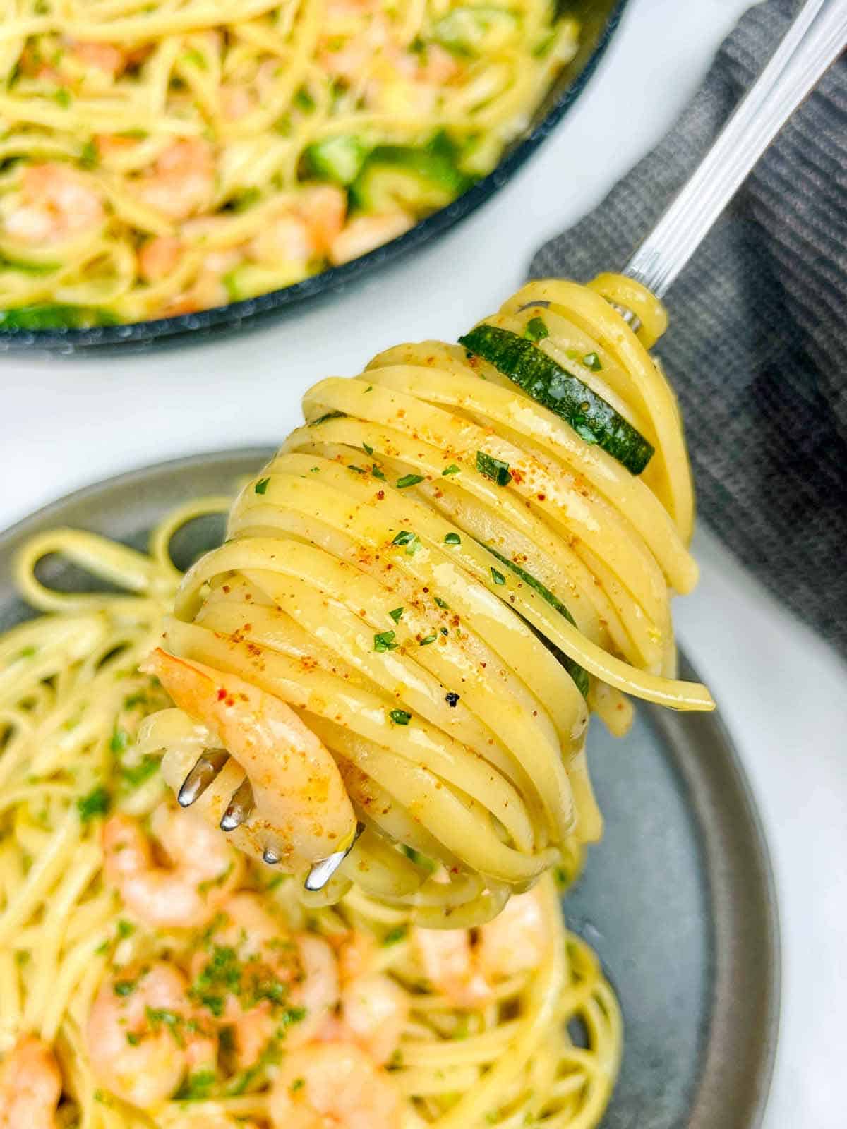 pasta dish : linguine with shrimp and zucchini on a fork. Pasta plate in the background.